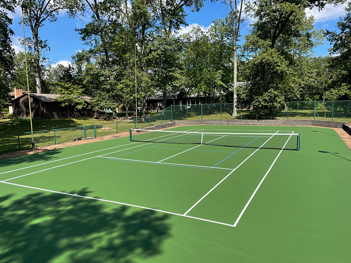 a resurfaced tennis court with trees and houses surrounding it