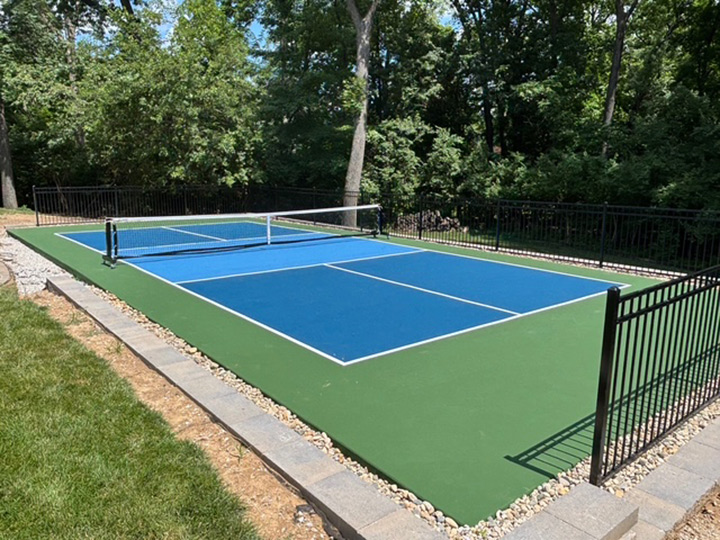 a resurfaced outdoor pickle ball court with green and multiple blue colors along with trees in the background